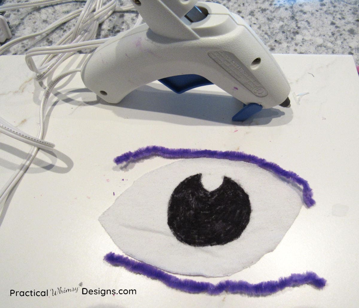 Gluing pipe cleaners on fabric eye with hot glue gun
