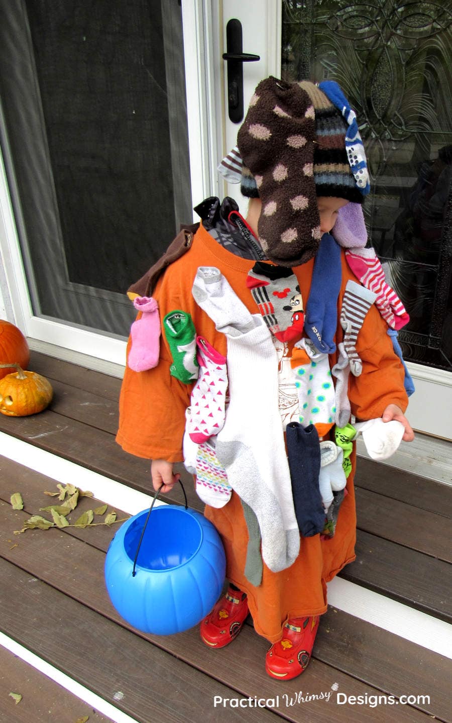 Little boy wearing DIY sock monster costume holding blue pumpkin bucket