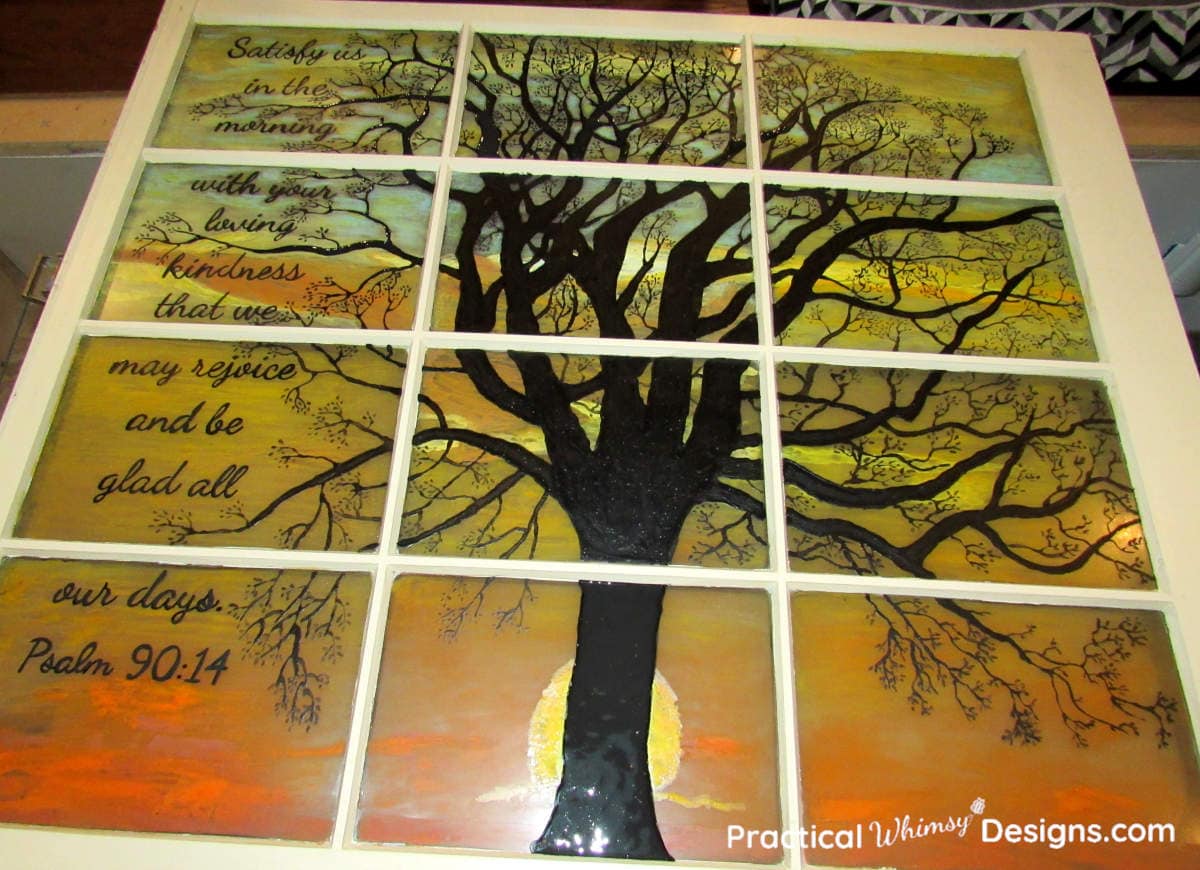 Black tree silhouette, sunrise, and verse on glass window.