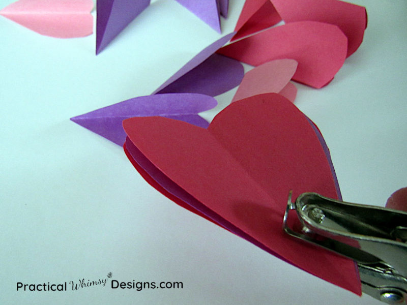 Using hole punch to punch holes in paper hearts
