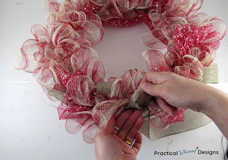 Hand pulling burlap ribbon loops through the deco mesh wreath frame.