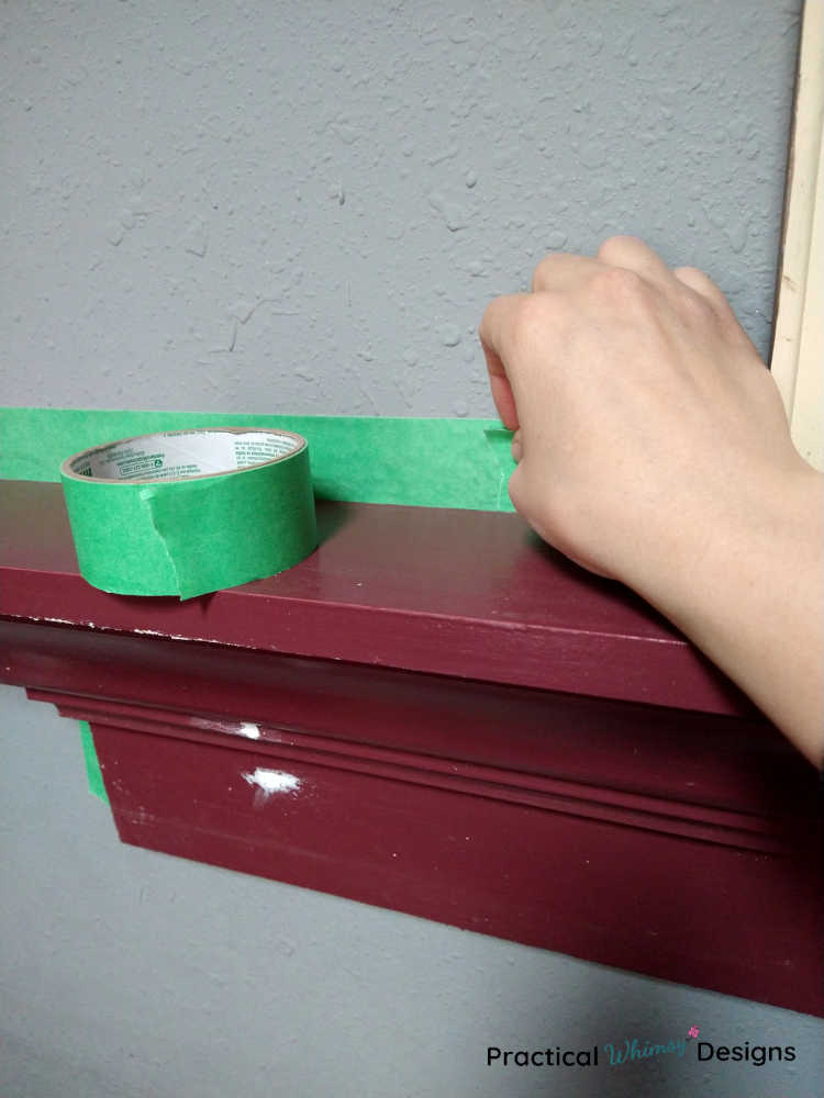 Taping the wall around a maroon shelf with painters tape