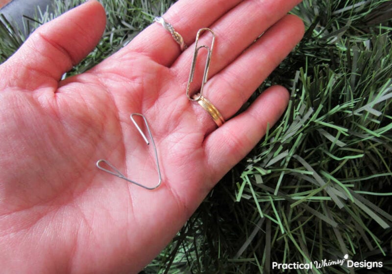 Hand holding paperclips bent into a hook shape.