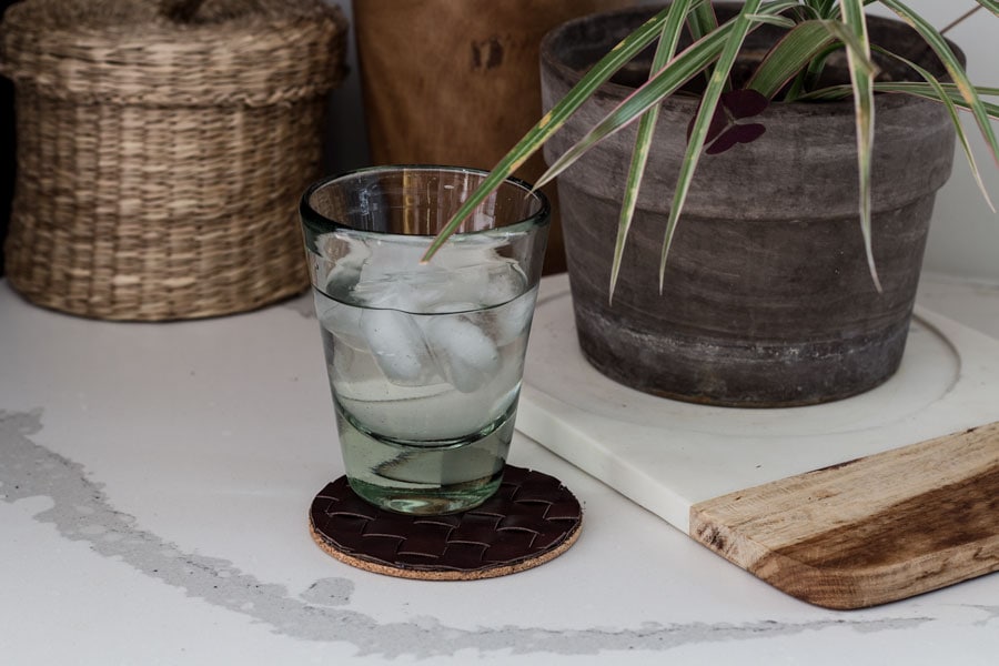 Woven leather coaster on table with glass of ice water