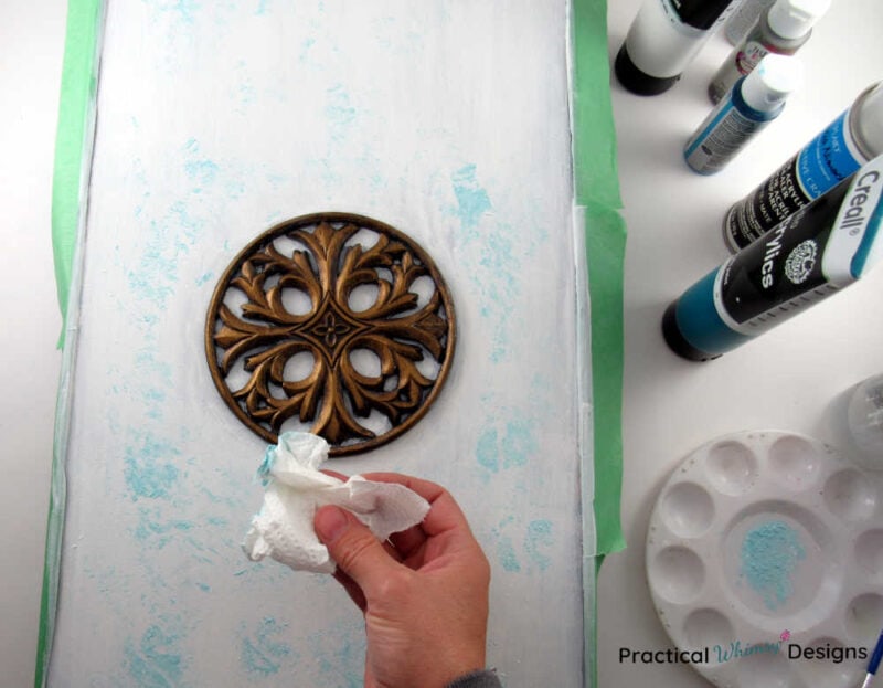 Blotting teal paint onto white picture with paper towel.