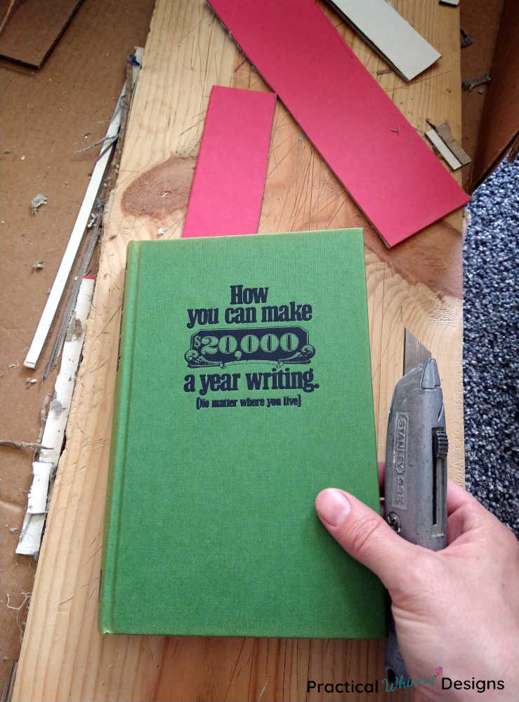 Hand holding a utility knife and green hardcover book.