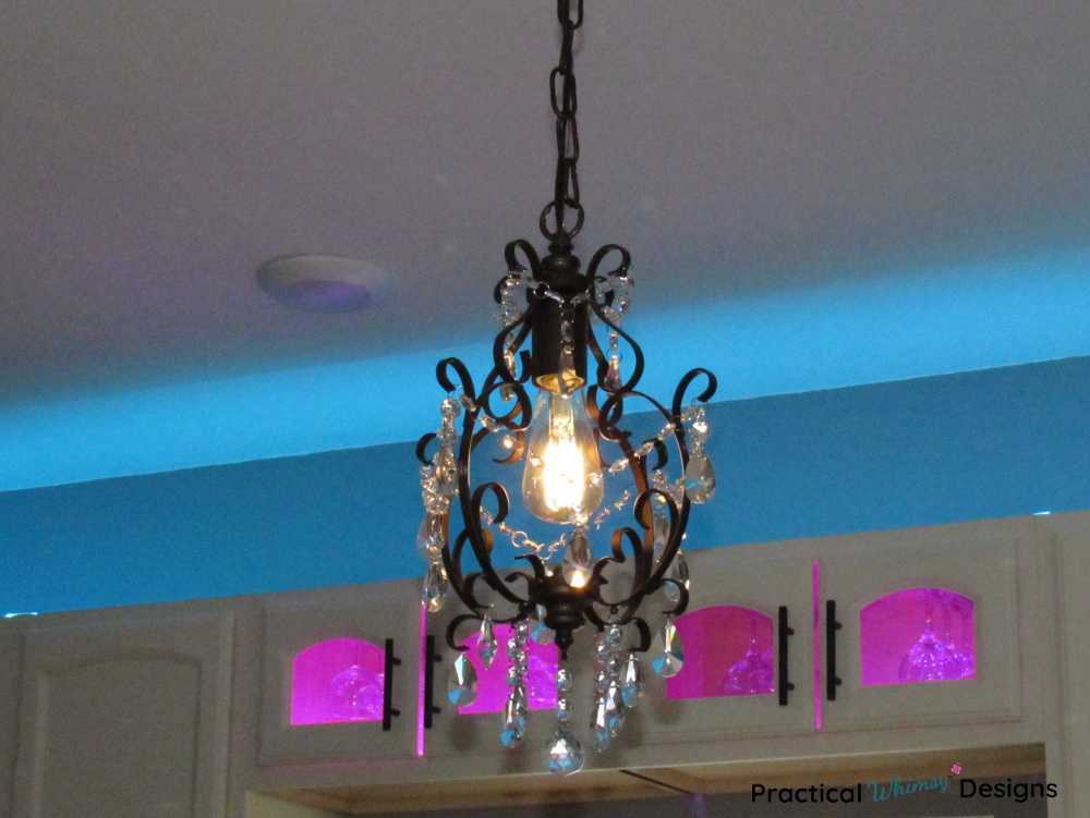 Glass chandelier in front of cabinets with pink and blue lighting