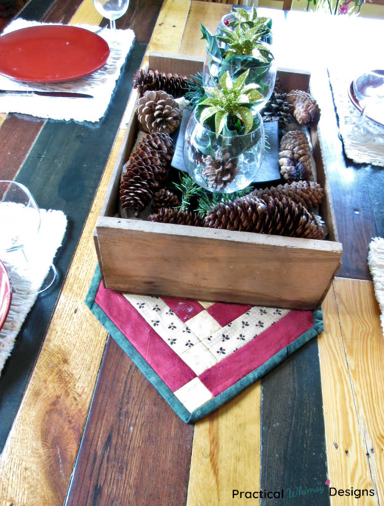 Christmas pinecone centerpiece sitting on runner next to red plate