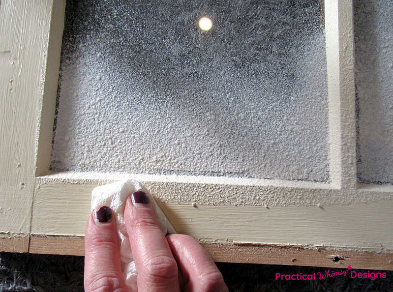 Hand wiping excess spray snow from the window frame.