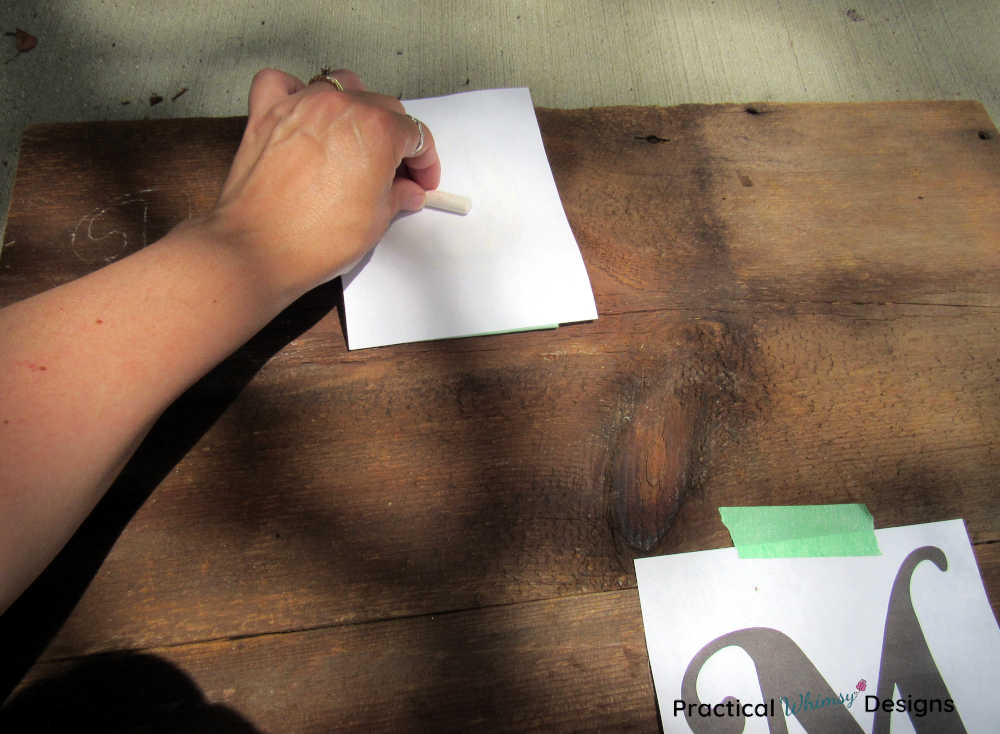 Coloring the back of the paper with chalk to transfer the lettering onto a wooden board.