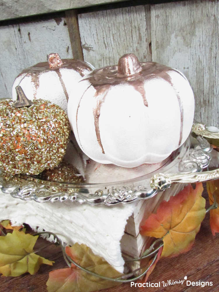 Copper dripped pumpkins and gold pumpkin on tray in front of rustic hearth wood.