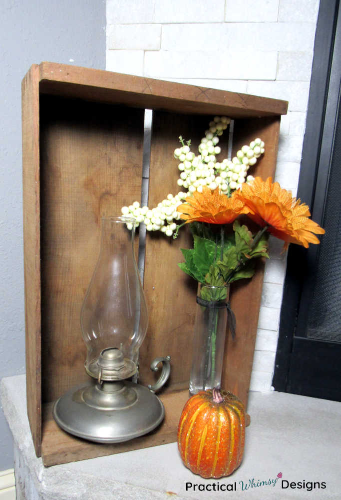 Crate, lamp, pumpkin, and fall flowers on hearth.