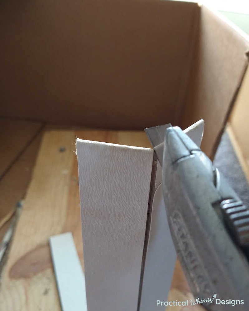 Utility knife cutting book cover into thin strips for faux bookshelf.