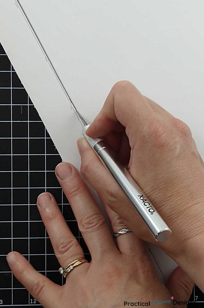 Hands using craft knife to cut white foam board into one inch strips.