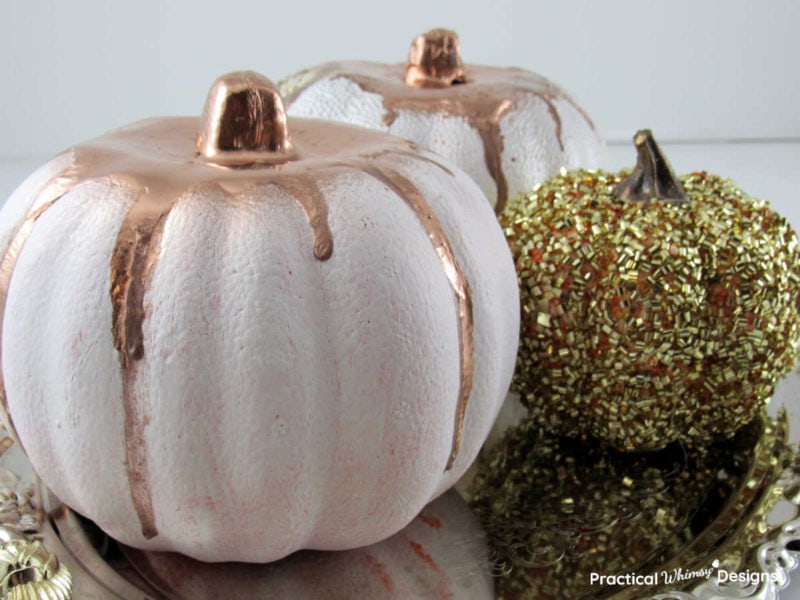 Copper dripped pumpkins and gold pumpkin sitting on a silver tray.