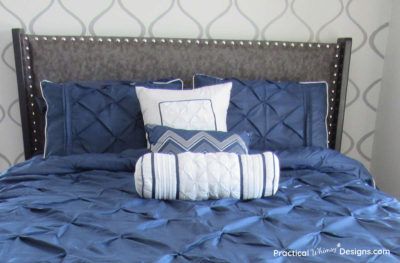 Bed with navy blue comforter, pillows, and fabric headboard