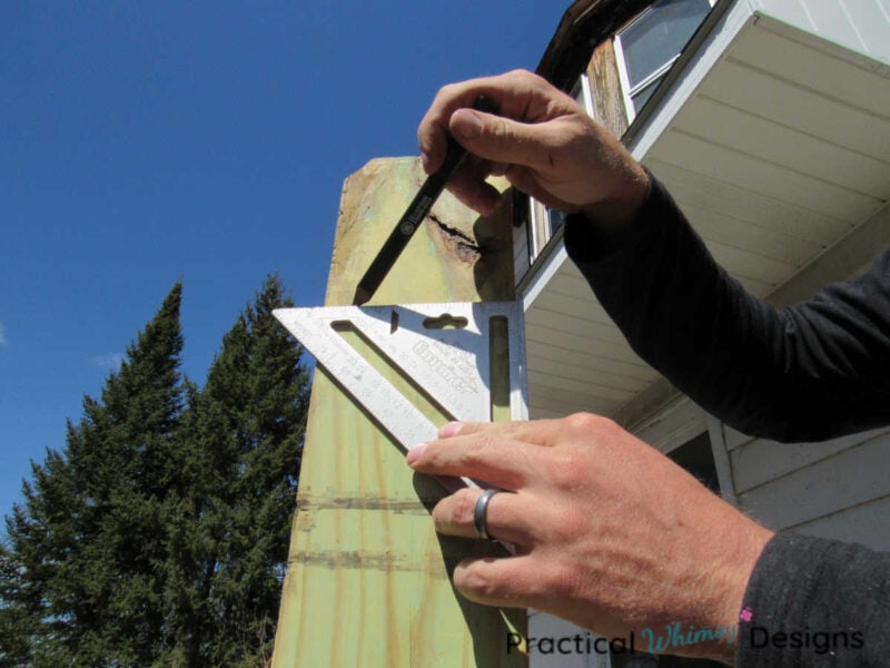 Drawing cutting line on pergola post with pencil and measuring square.