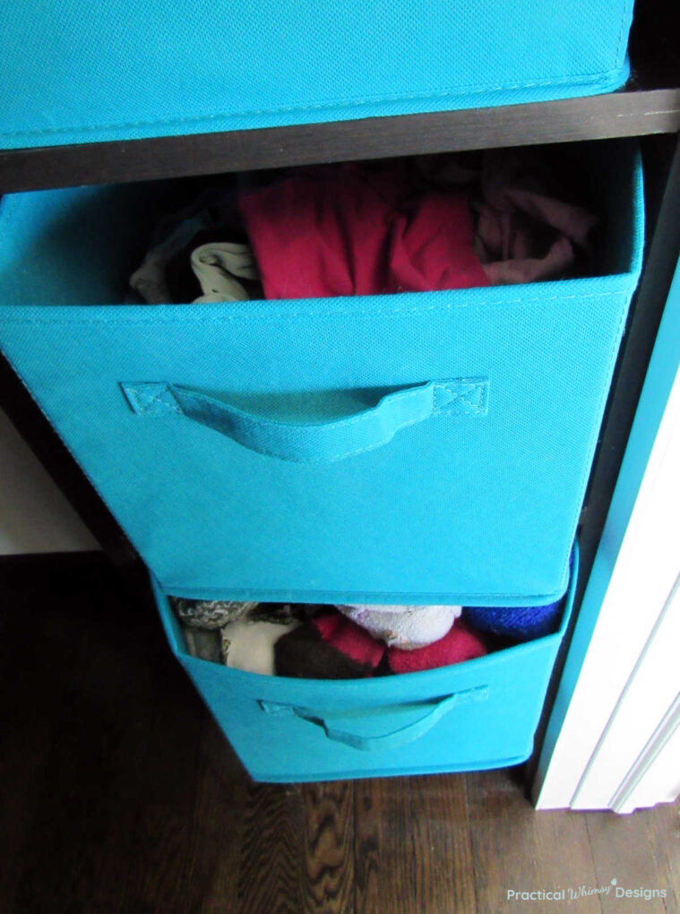 Underwear and socks stored in teal fabric boxes on shelf in closet.