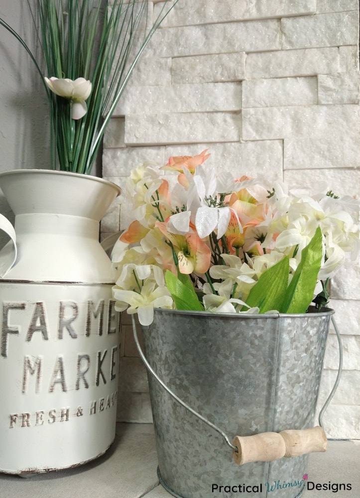 White milk just and silver bucket with faux flowers on mantel.