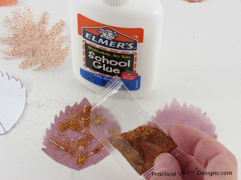 Sprinkling glitter on glue on decorative fall leaf