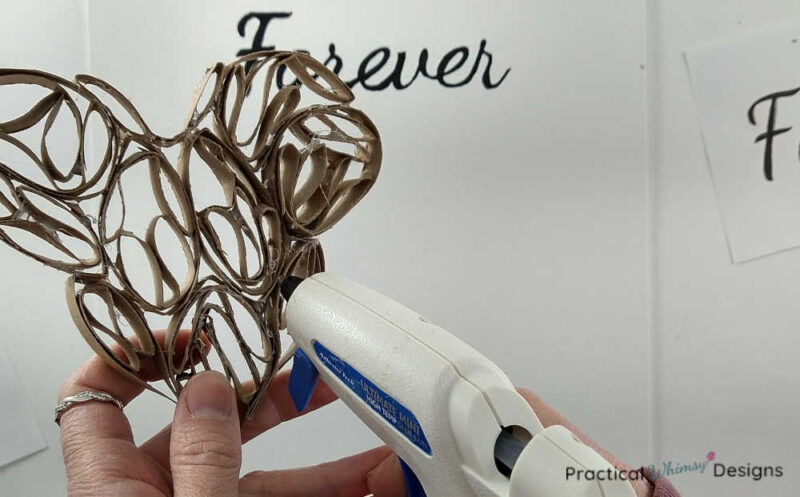 Gluing 3D paper heart onto canvas with hot glue gun.