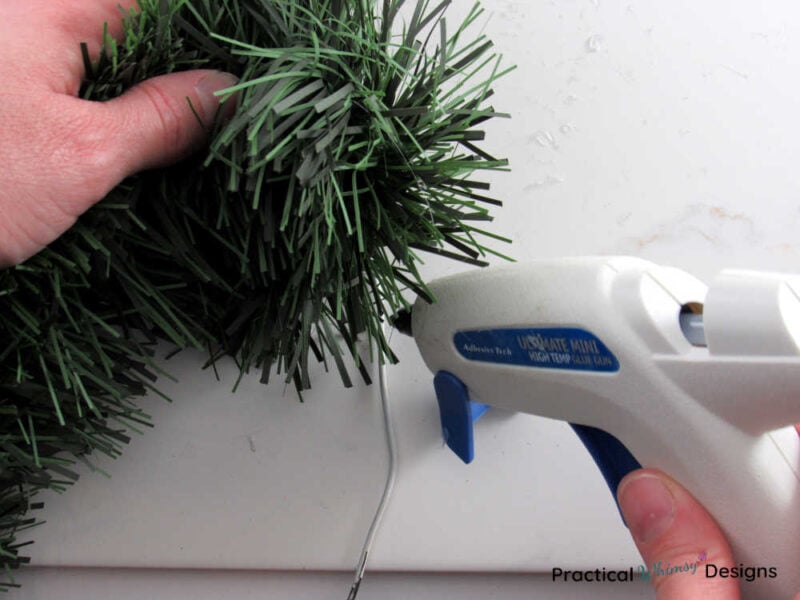 Hands hot gluing pine garland onto wire