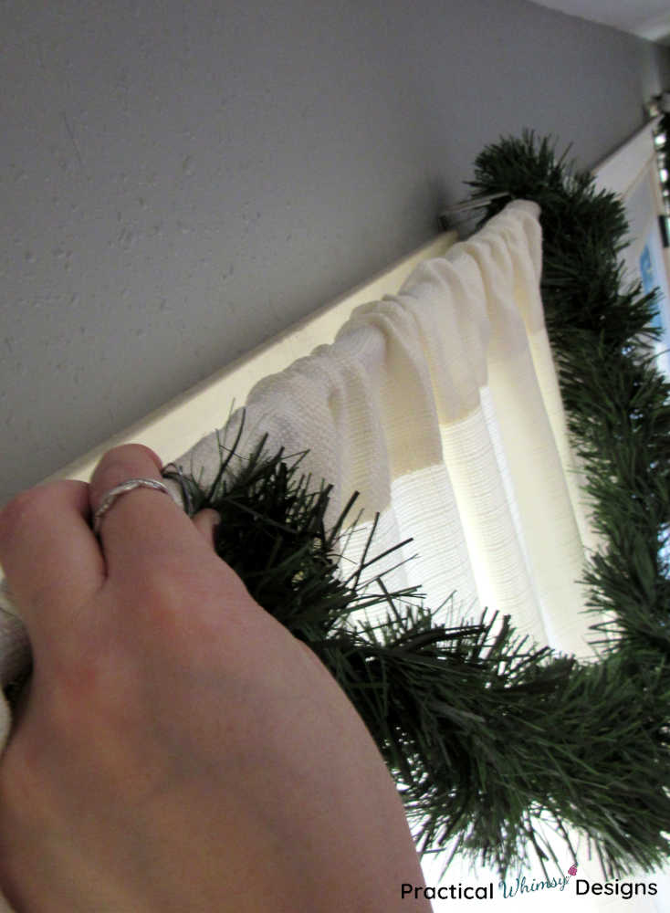 Hooking pine garland onto the center of a white curtain.
