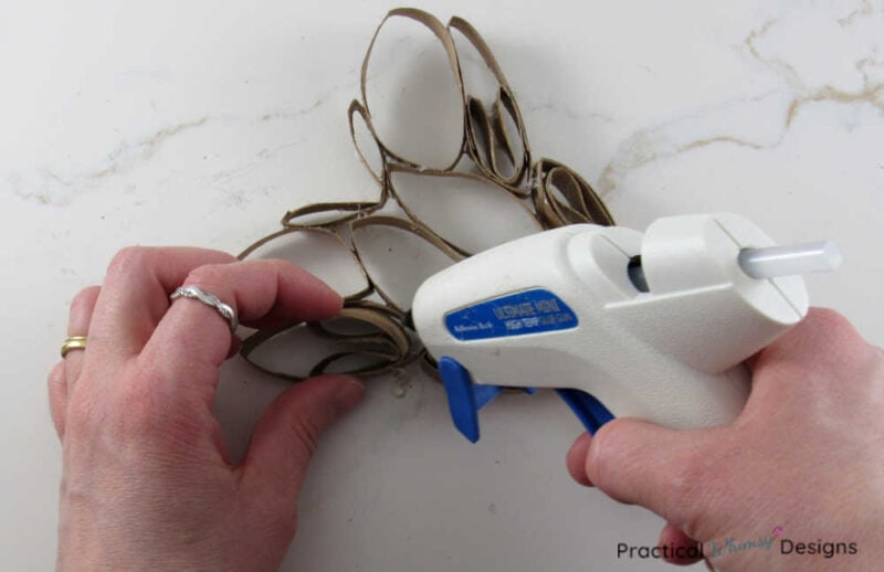 Gluing toilet paper roll segments into paper heart with hot glue gun.