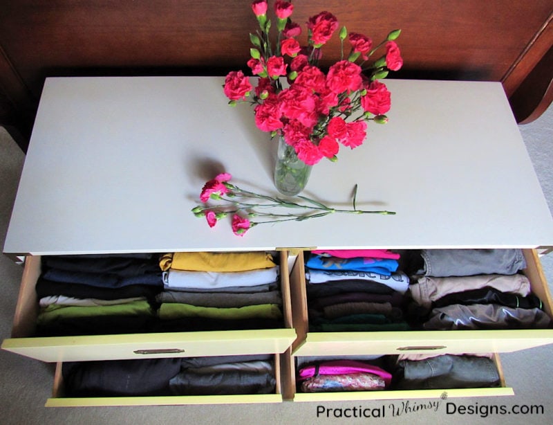 Organized clothes drawers with pink flowers on top of white dresser.