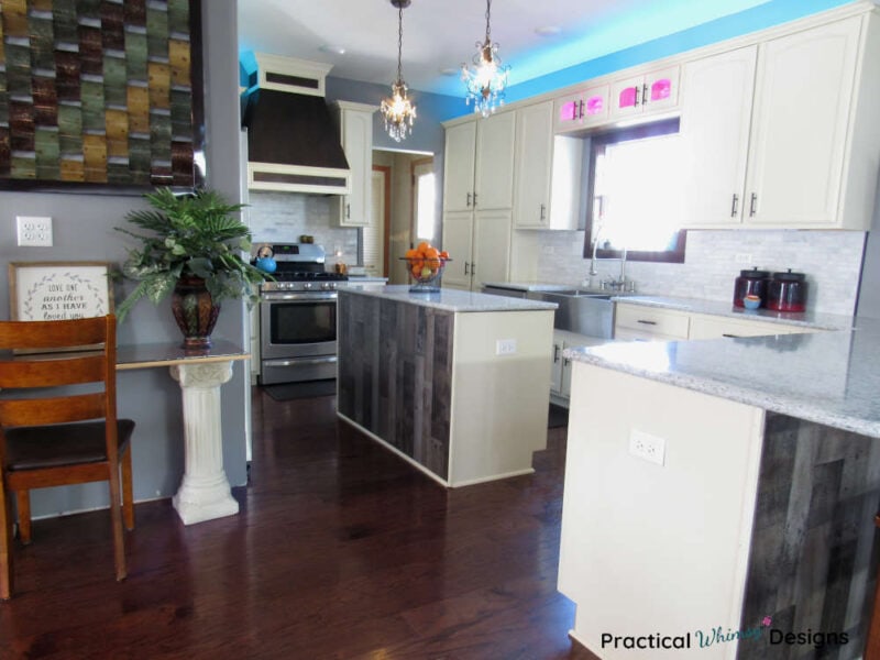 Full kitchen reveal with white cabinets, wood flooring, tile backsplash, and white quartz counters