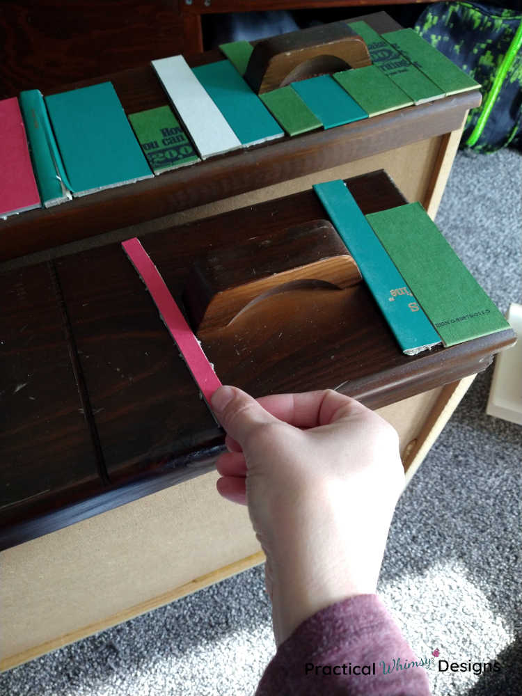 Hand setting red book end on dresser to measure faux book shelf spacing.