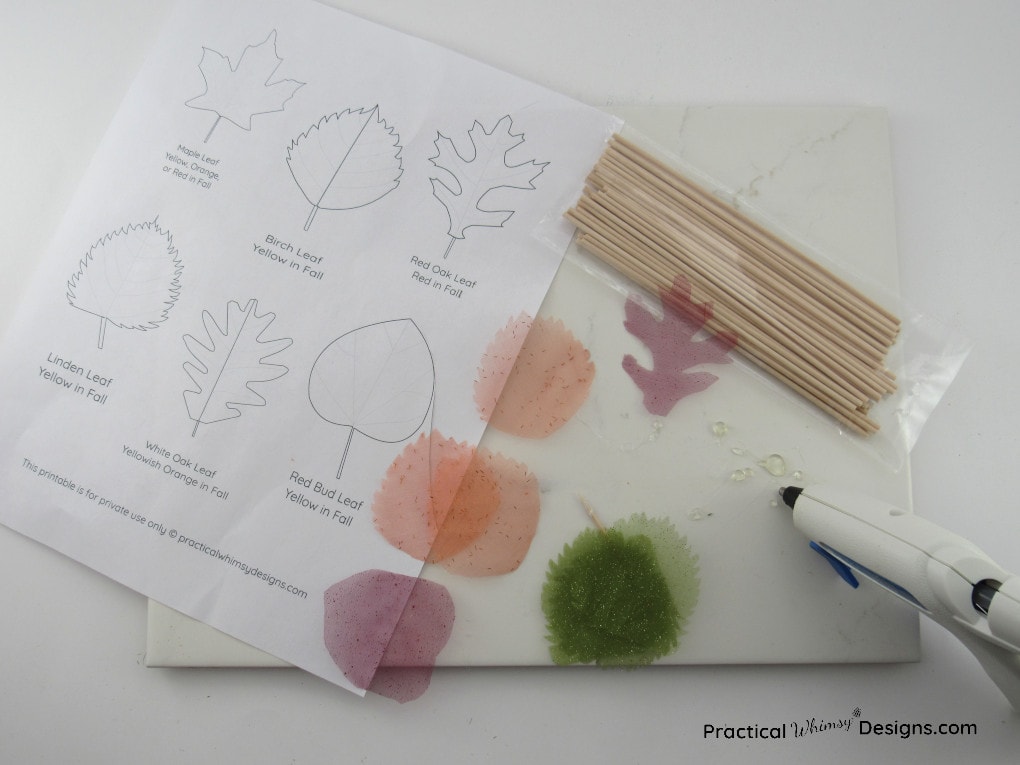 Supplies for making fabric flowers out of fall leaves: fabric leaves, hot glue, wooden dowels, and leaf template.