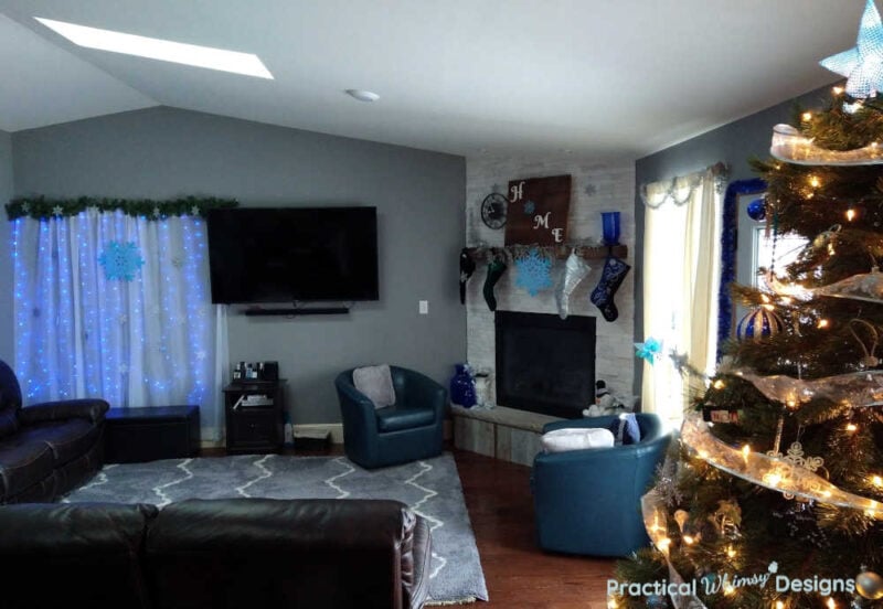 Family room decorated with Christmas tree, stockings on mantel, and lighted curtain.