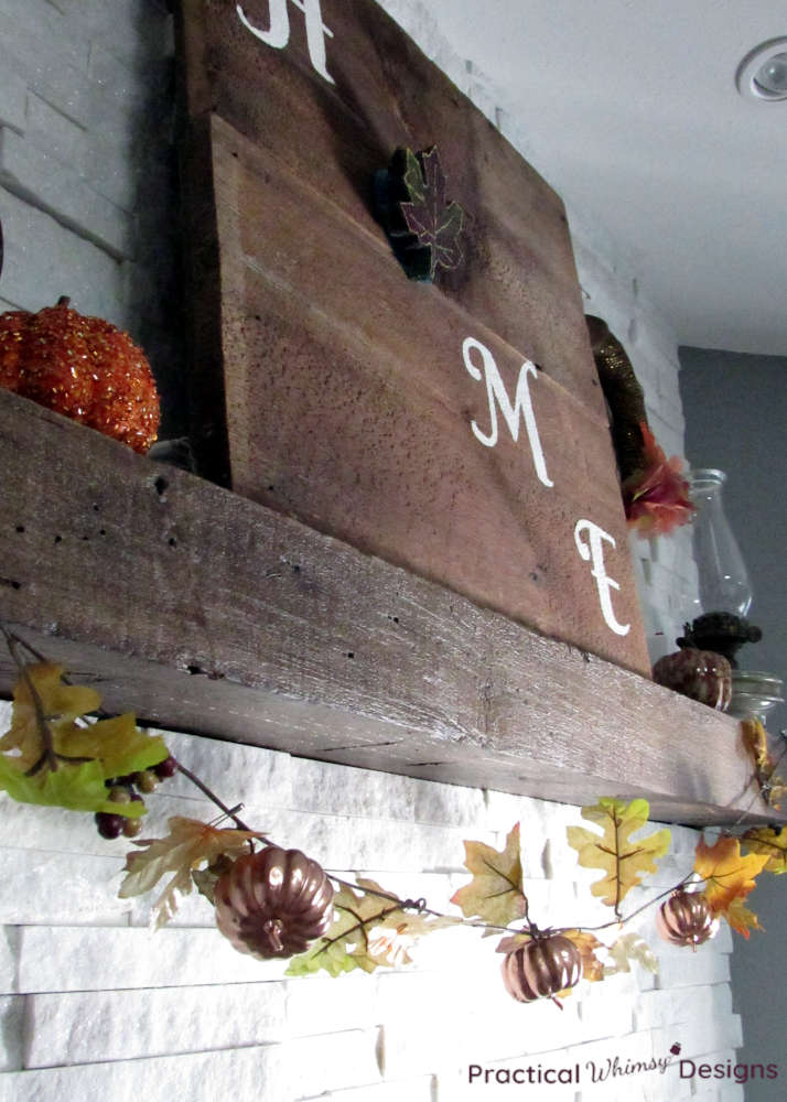 Rustic home sign with pumpkins and leaf garland on mantel.