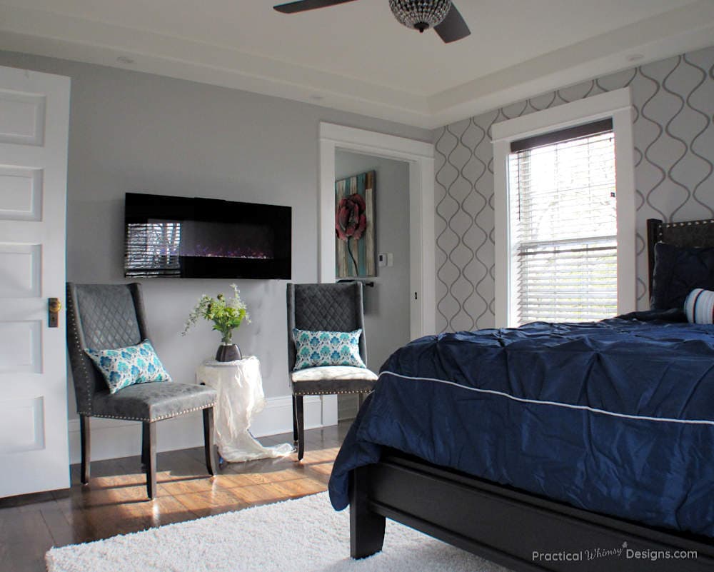 Master bedroom with gray stenciled wall, electric fireplace and gray chairs