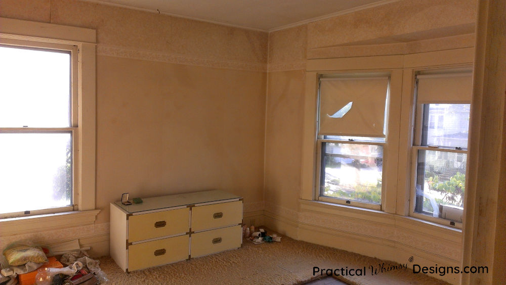 Master bedroom before remodeling with stained wall paper and cracked windows.