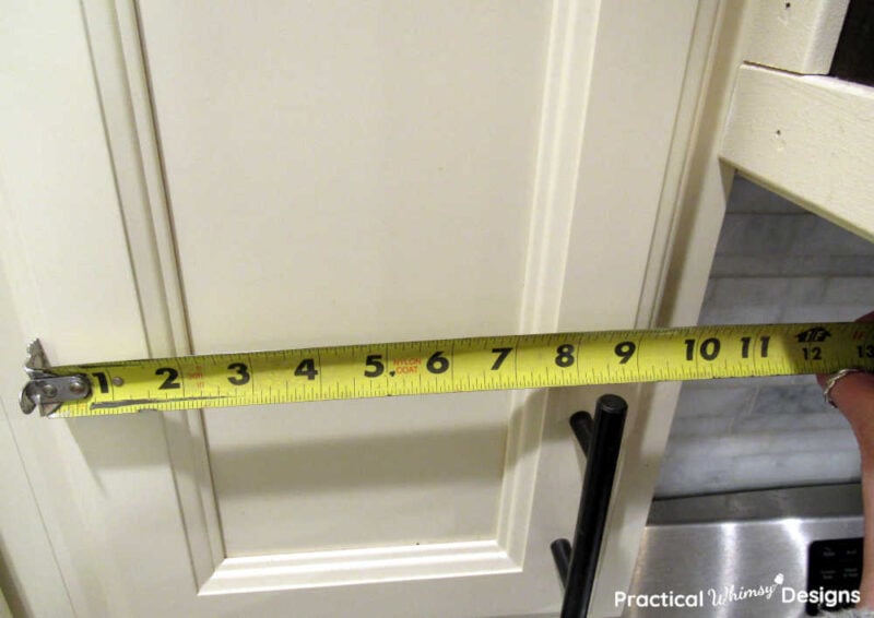 Measuring tape measuring width of kitchen cabinet.