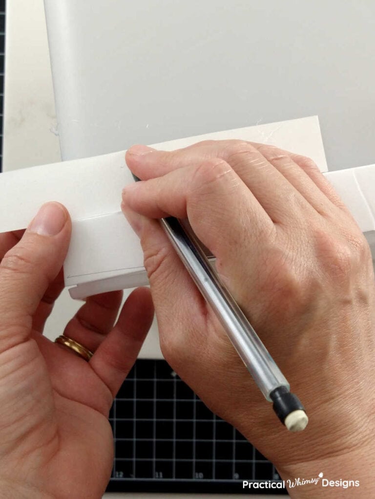 Hands marking a cut mark on poster board with a pencil to indicate where to cut.