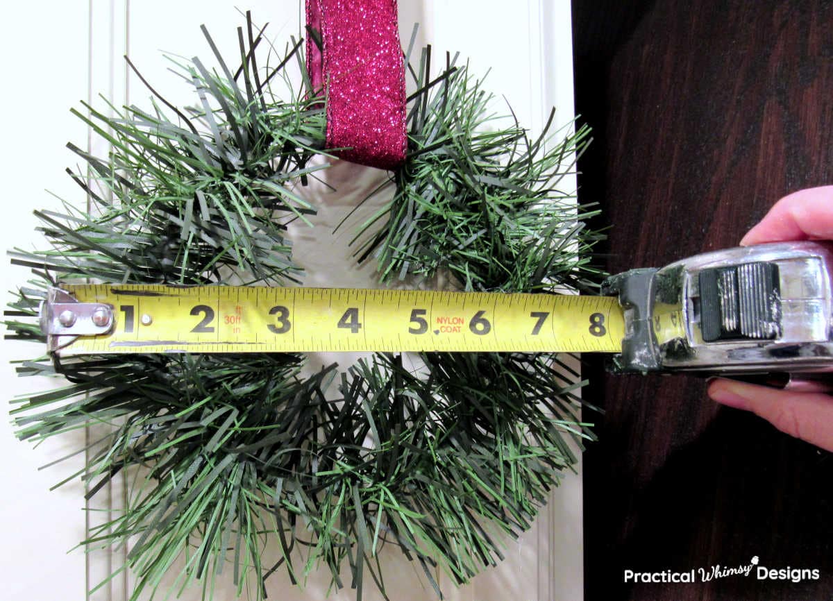 Measuring tape measuring size of wreath hanging on kitchen cabinets.