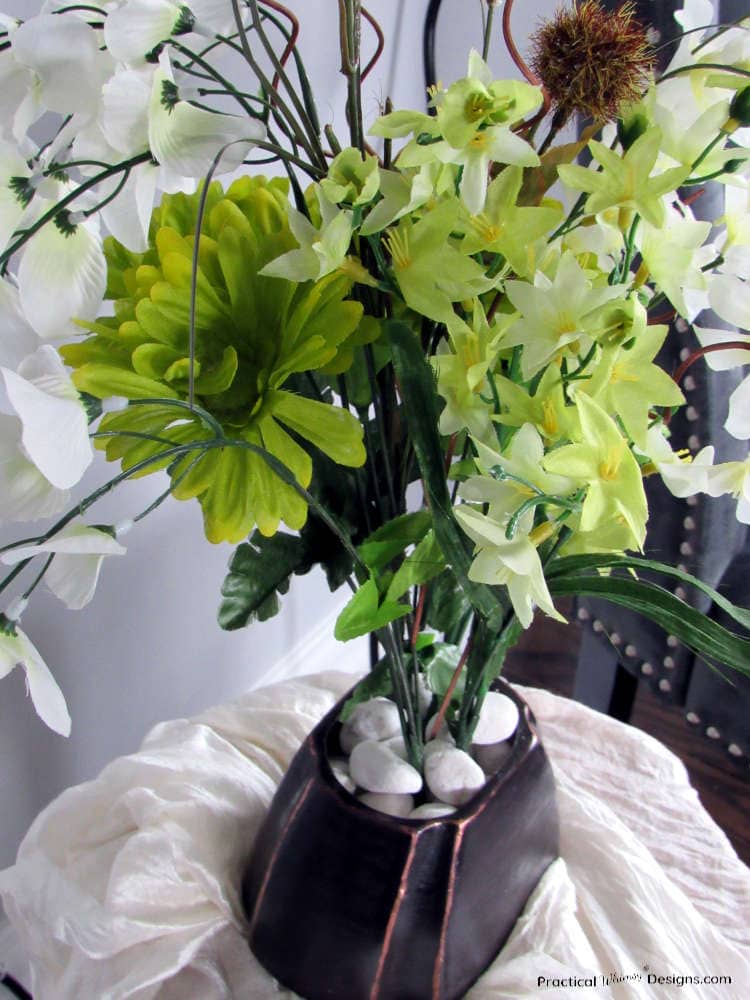 Ceramic vase painted like oil rubbed bronze with green and white flowers in it.