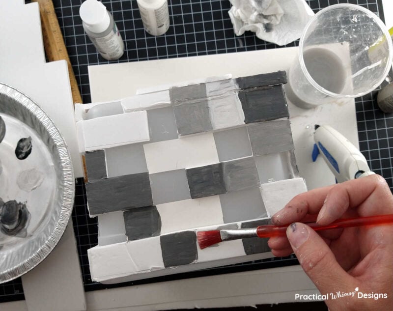 Painting different shades of grey squares with acrylic paint on the pixelated brick video game light.