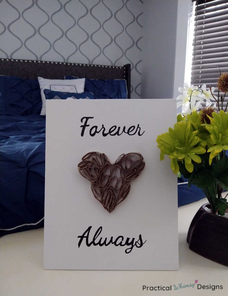 Heart toilet paper roll art next to bed and green flowers in vase