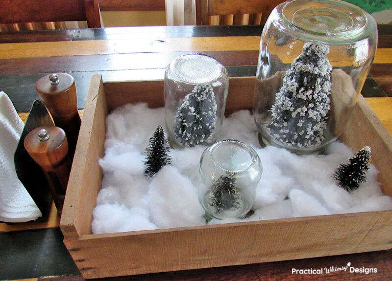 Pine tree snow globes in crate on dinning room table.