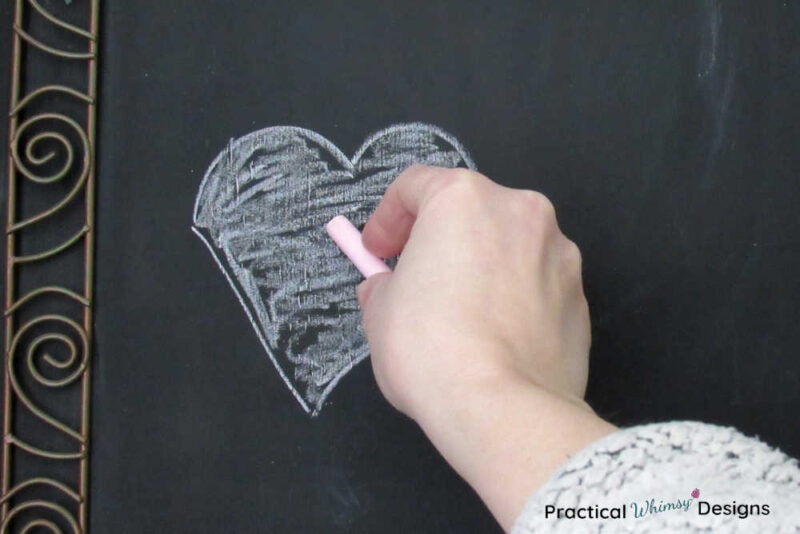 Hand drawing pink chalk heart on chalkboard