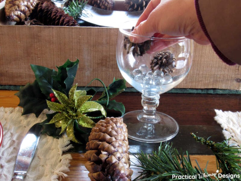 Hand placing small pinecone in wine glass