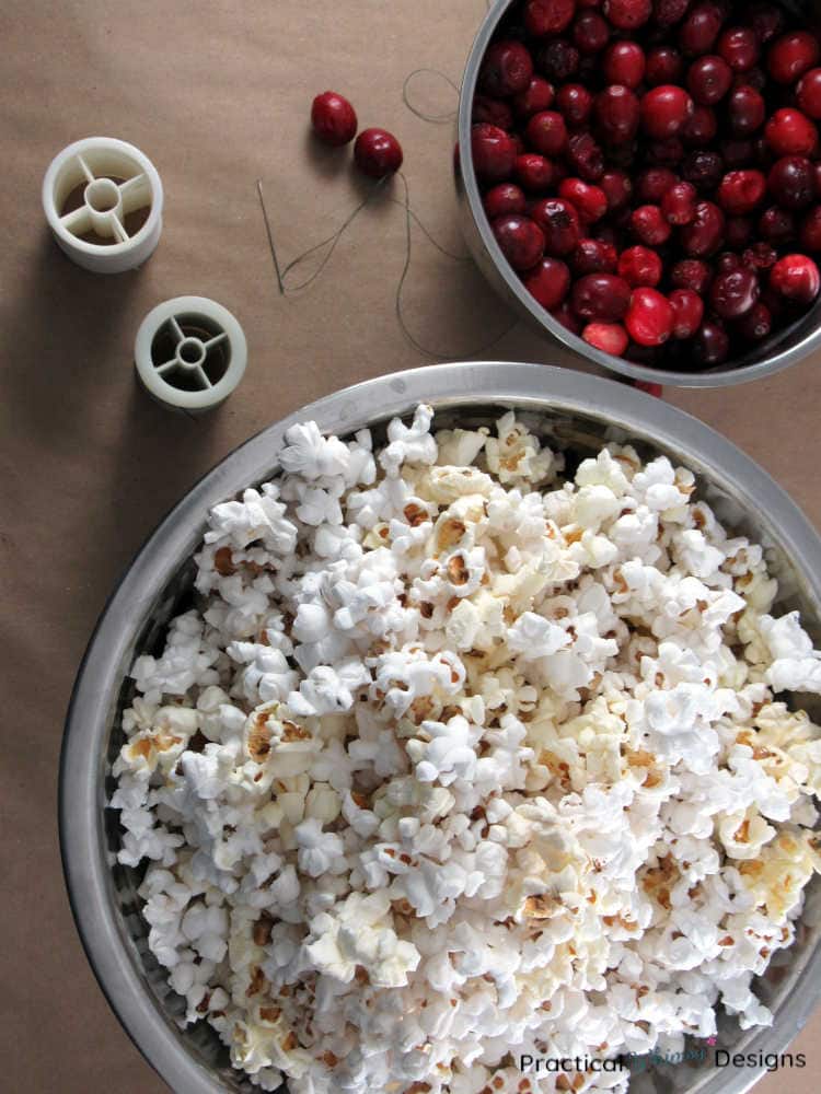 Cranberries and popcorn filled bowls next to thread spools.