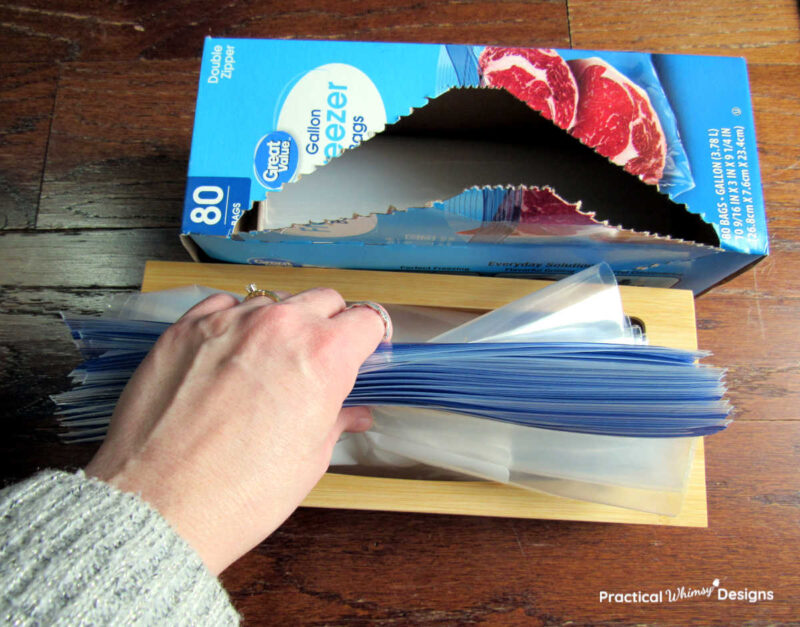 Hand placing ziplock storage bags in bamboo bag storage container.