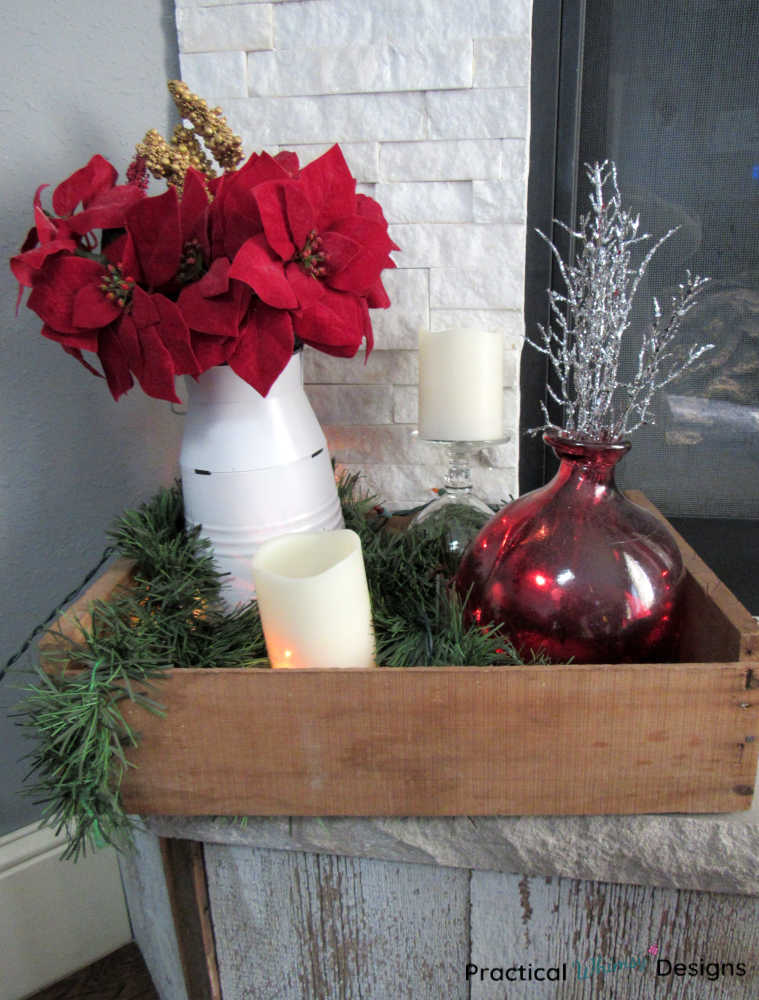 Red poinsettias, candles, and greenery in a wooden crate.