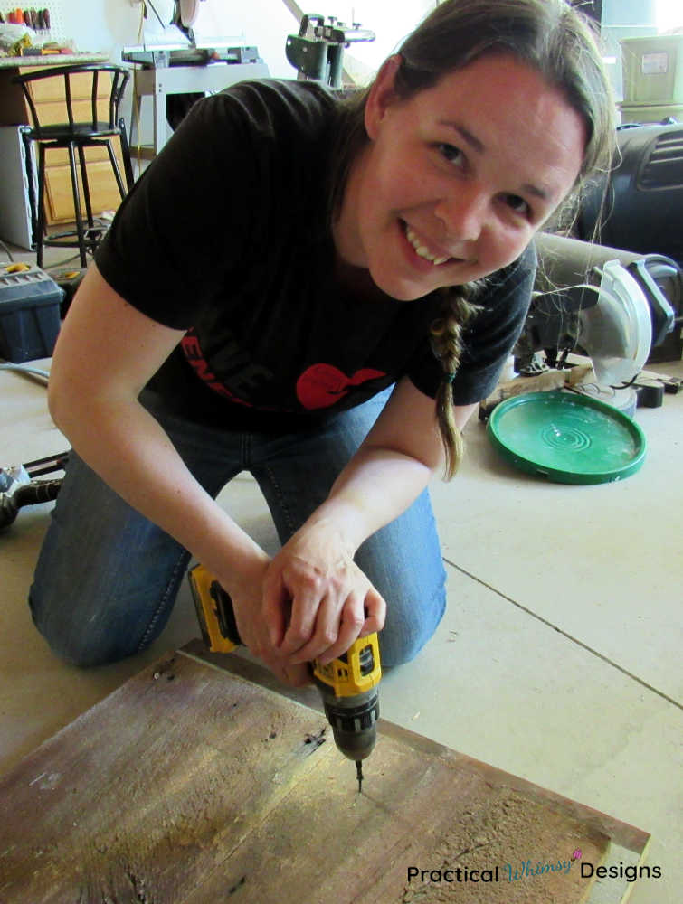 Lady smiling as she screws boards together to make a wooden home sign.