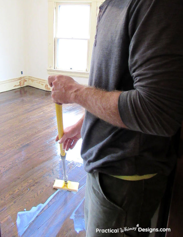 Man spreading polyurethane on the wooden floor.